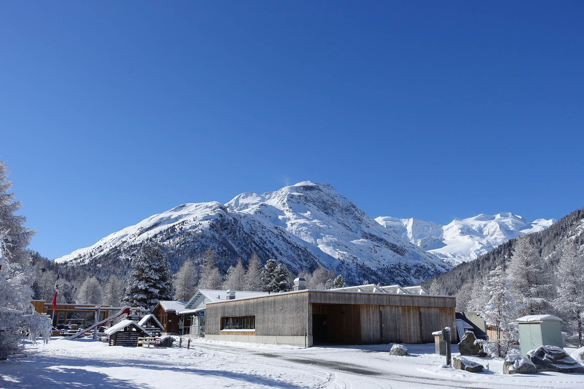 Frisch verschneites Sanitärgebäude mit der dazugehörigen Frischwasser und Grawasser-Station. Im Hintergrund das Rezeptionsgebäude, das Restaurant und der Spielplatz